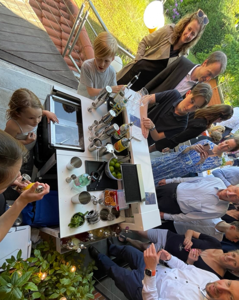 Um die Break Pop-Up Bar gesellen sich viele Erwachsene und Kinder, um der Barkeeperin beim Cocktail Catering zuzusehen und die Cocktails zu genießen.